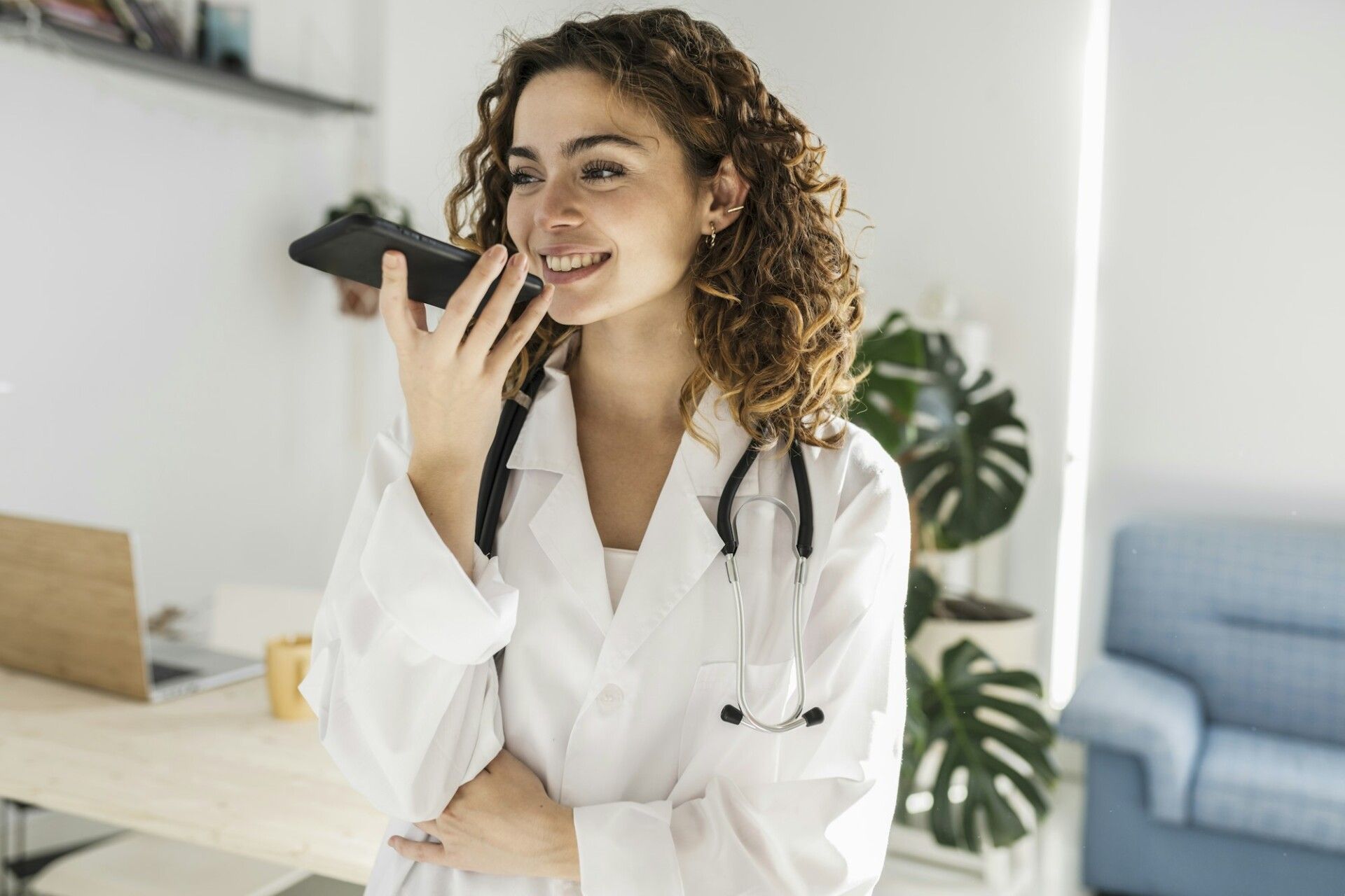 Young curly haired female doctor sending an audio message to a patient with her smartphone