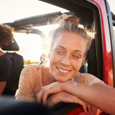 Millennial white couple on a road trip driving in open top car, women leaning on car door, close up